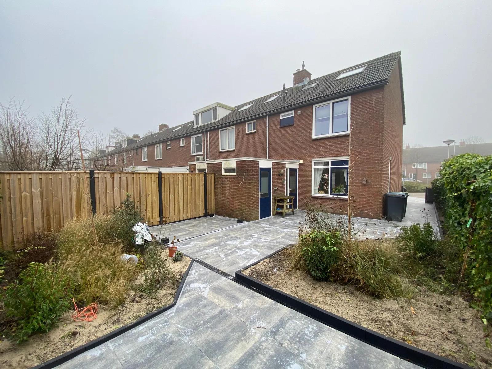 Nieuwe bestrating voor een rij woningen met houten schuttingen